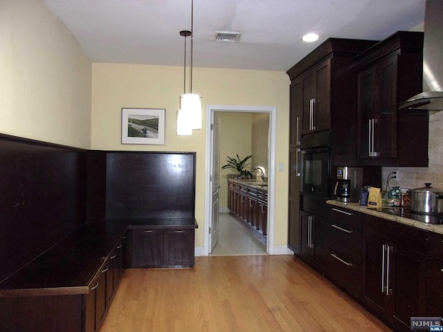 kitchen with black appliances, visible vents, light wood-style floors, and wall chimney range hood