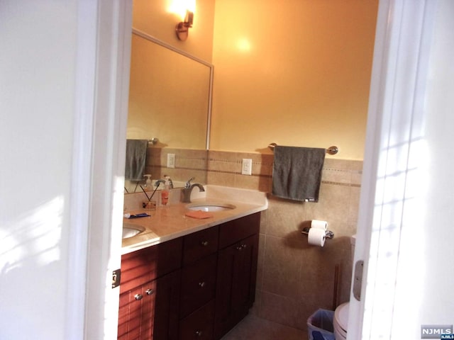 full bathroom featuring double vanity, a wainscoted wall, tile walls, and a sink