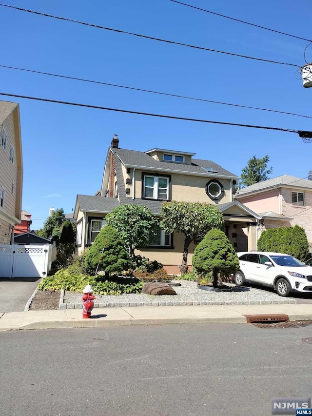 american foursquare style home featuring driveway, a chimney, fence, and stucco siding