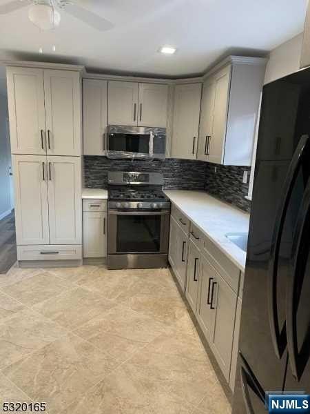 kitchen with backsplash, gray cabinets, ceiling fan, and stainless steel appliances