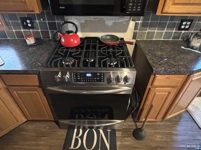 kitchen featuring backsplash, dark stone counters, stainless steel stove, and dark wood-type flooring