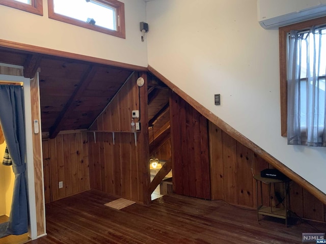 interior space with a wall unit AC, a wealth of natural light, wood-type flooring, and lofted ceiling