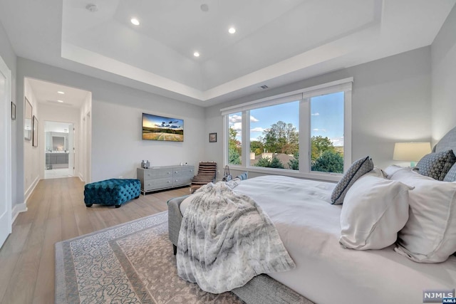 bedroom with light hardwood / wood-style floors and a raised ceiling