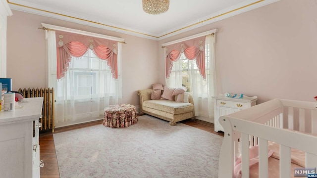 bedroom with radiator heating unit, a nursery area, crown molding, and hardwood / wood-style floors