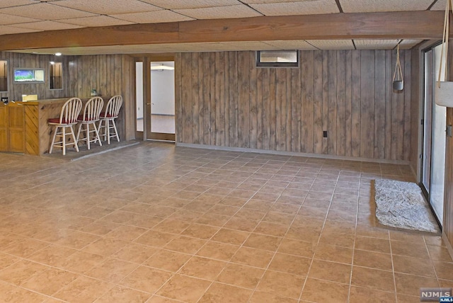 basement featuring a paneled ceiling and wood walls