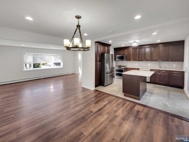 kitchen with tasteful backsplash, light hardwood / wood-style flooring, pendant lighting, a kitchen island, and appliances with stainless steel finishes