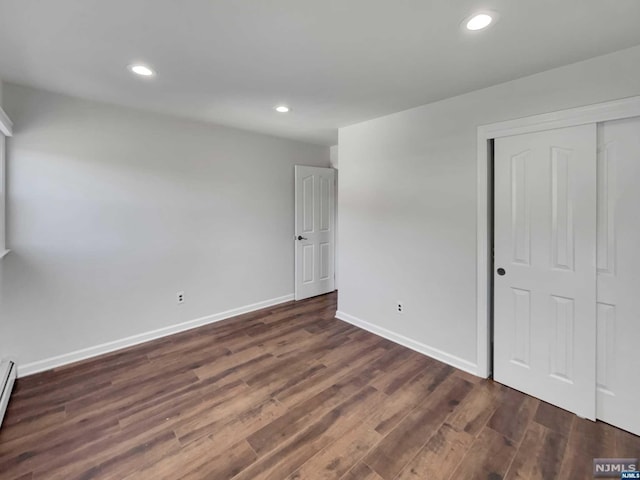 unfurnished bedroom with a baseboard heating unit, a closet, and dark wood-type flooring