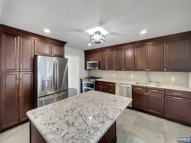 kitchen featuring sink, decorative backsplash, a kitchen island, light stone counters, and stainless steel appliances