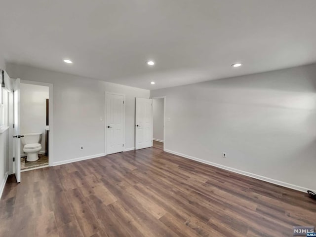 unfurnished bedroom featuring ensuite bathroom and dark hardwood / wood-style flooring