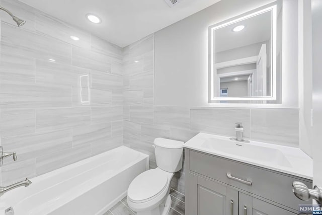 full bathroom featuring vanity, tiled shower / bath combo, tile walls, and toilet