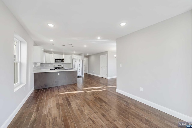 kitchen featuring dark hardwood / wood-style flooring, backsplash, stainless steel appliances, white cabinets, and hanging light fixtures