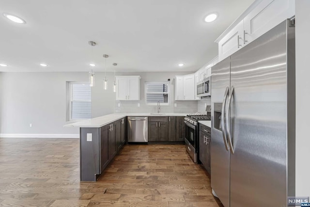 kitchen with sink, hanging light fixtures, stainless steel appliances, kitchen peninsula, and hardwood / wood-style flooring