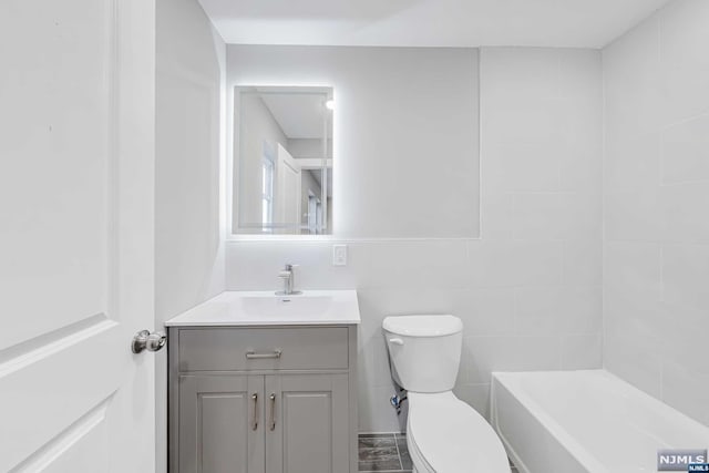 bathroom featuring a bathtub, vanity, tile walls, and toilet