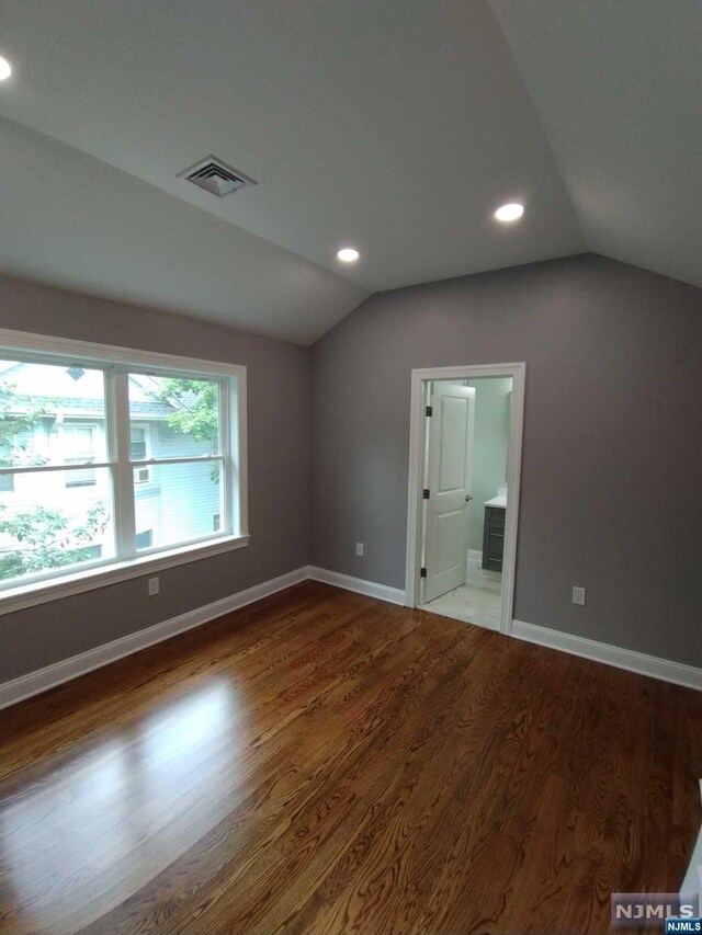 unfurnished bedroom featuring wood-type flooring, ensuite bathroom, and lofted ceiling