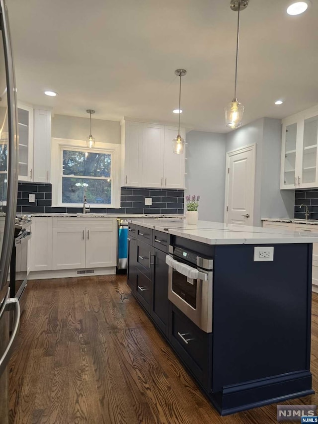 kitchen featuring white cabinets, appliances with stainless steel finishes, decorative light fixtures, and dark wood-type flooring