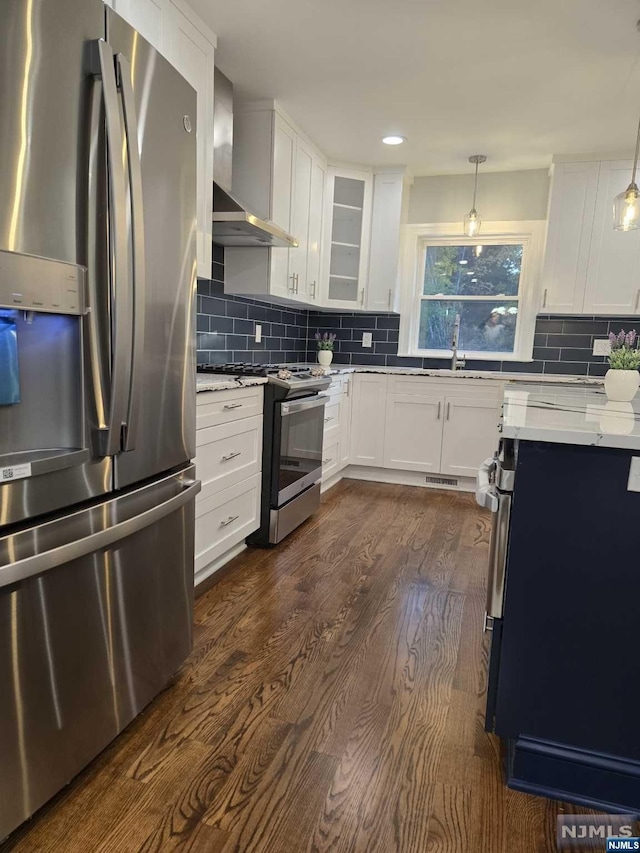 kitchen with white cabinetry, wall chimney exhaust hood, stainless steel appliances, and decorative light fixtures