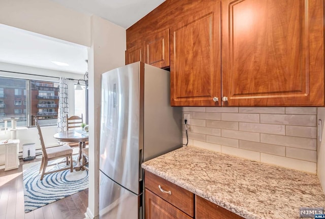 kitchen with hardwood / wood-style floors, stainless steel fridge, light stone countertops, and tasteful backsplash