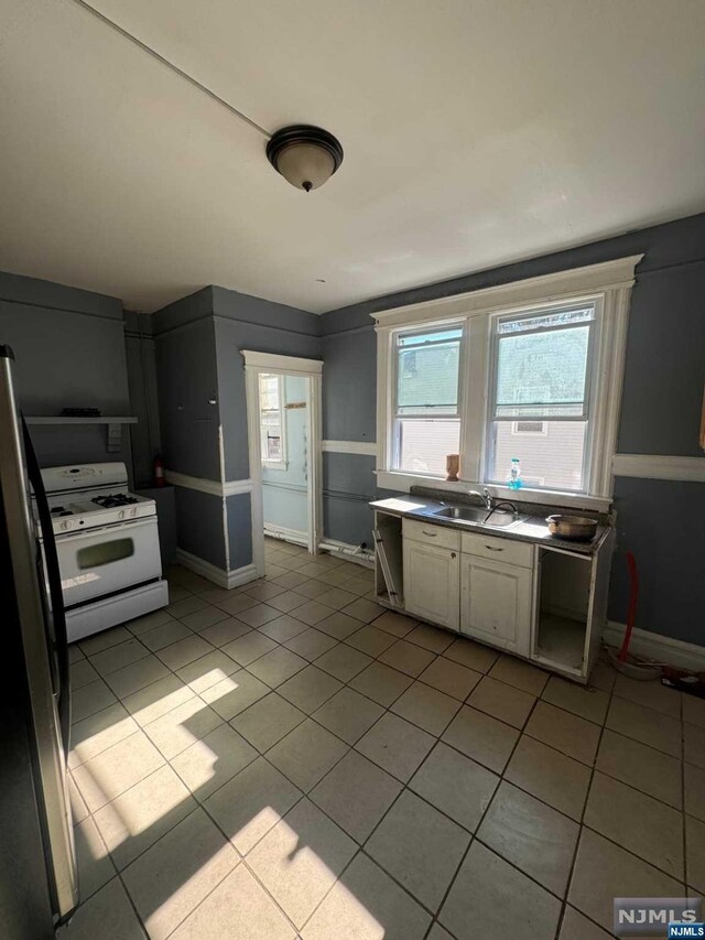 kitchen featuring sink, white gas stove, light tile patterned floors, and stainless steel fridge