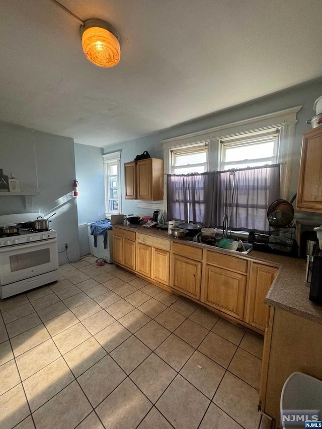 kitchen with sink, light tile patterned floors, white gas range, and plenty of natural light