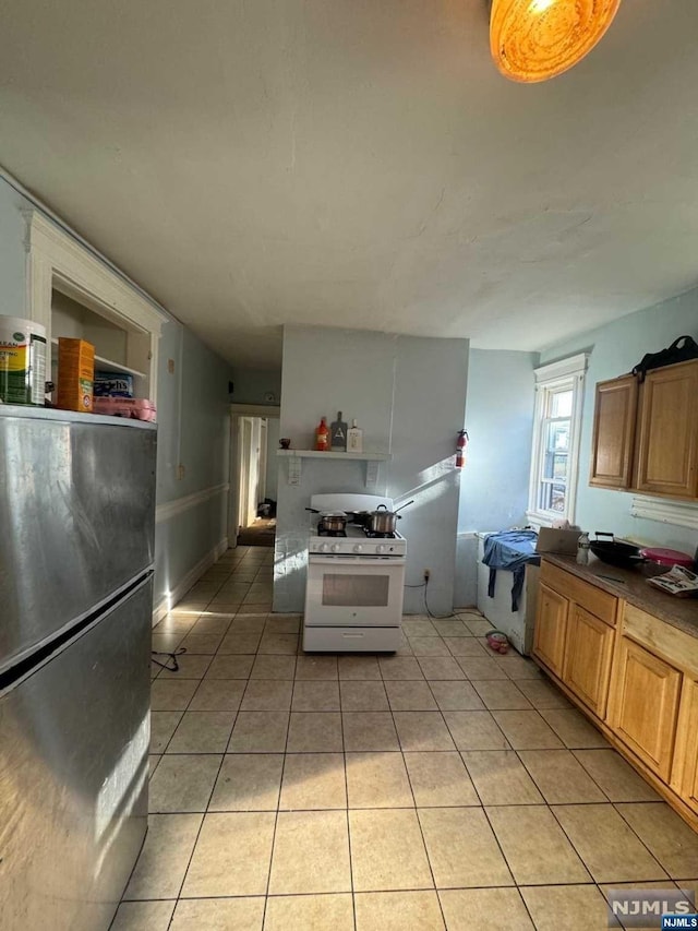 kitchen with white gas stove, light tile patterned floors, and stainless steel fridge