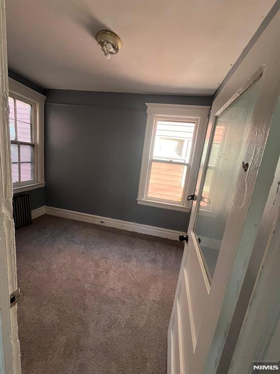 empty room with radiator heating unit, a healthy amount of sunlight, and dark colored carpet