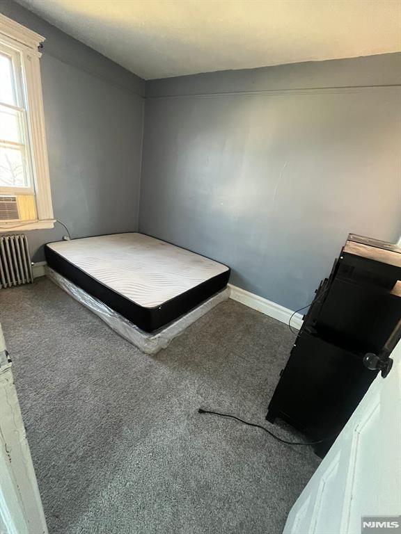 unfurnished bedroom featuring dark carpet and radiator heating unit