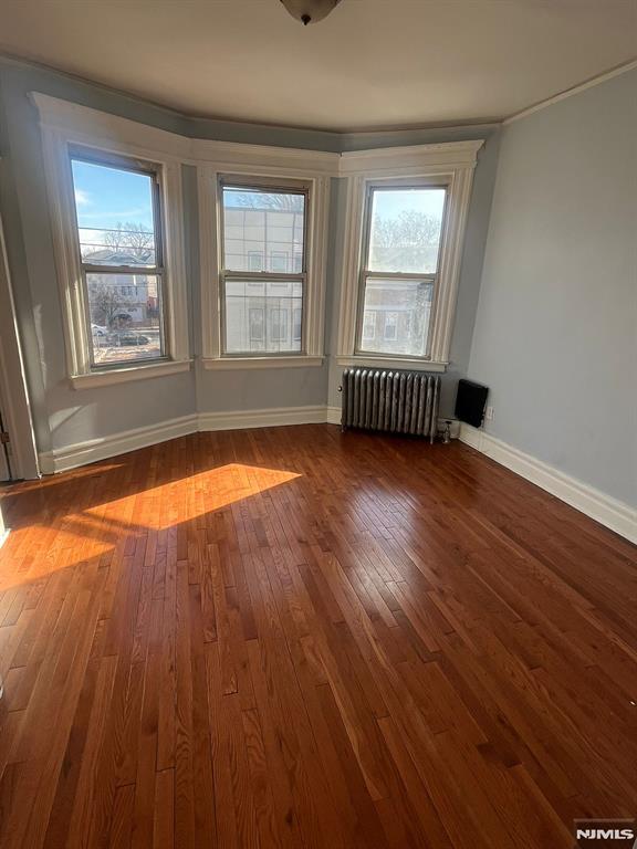 empty room with radiator heating unit and dark wood-type flooring