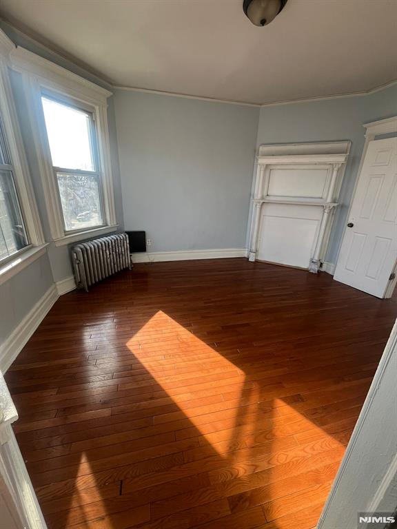 empty room with dark wood-type flooring and radiator heating unit