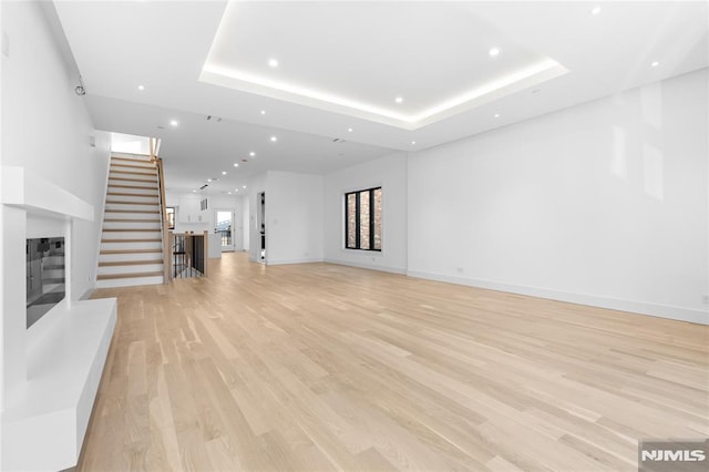 unfurnished living room with a tray ceiling and light hardwood / wood-style flooring