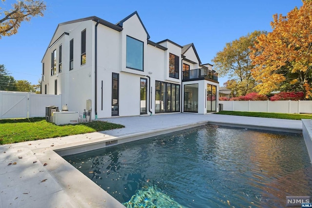 back of property featuring a balcony, a patio area, a fenced in pool, and central air condition unit