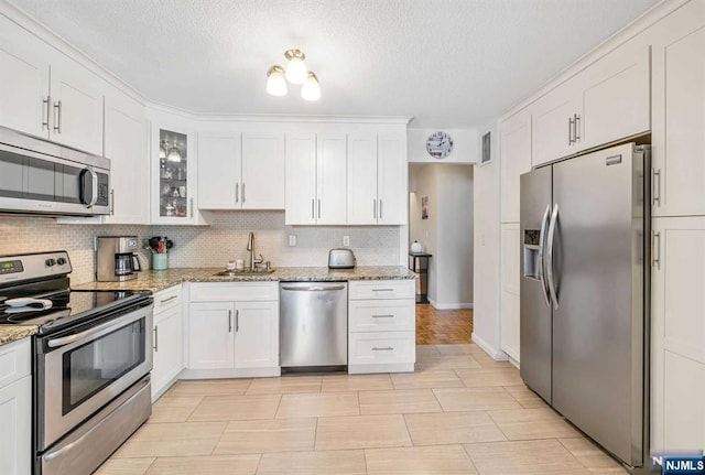 kitchen featuring light stone counters, stainless steel appliances, decorative backsplash, white cabinetry, and sink