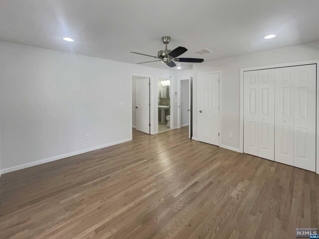 unfurnished bedroom featuring hardwood / wood-style floors, ceiling fan, connected bathroom, and two closets