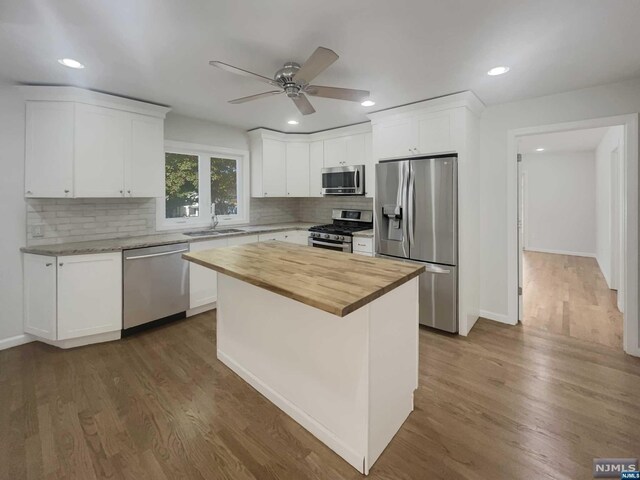 kitchen with white cabinets, appliances with stainless steel finishes, a center island, and dark hardwood / wood-style floors