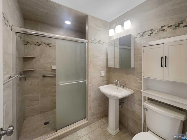 bathroom with tile patterned floors, a shower with shower door, tile walls, and toilet