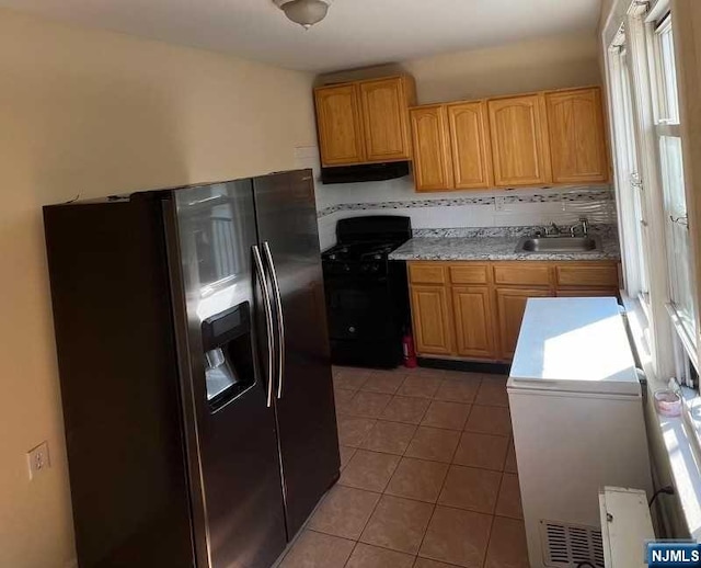 kitchen featuring stainless steel fridge, black gas range, a wealth of natural light, and sink