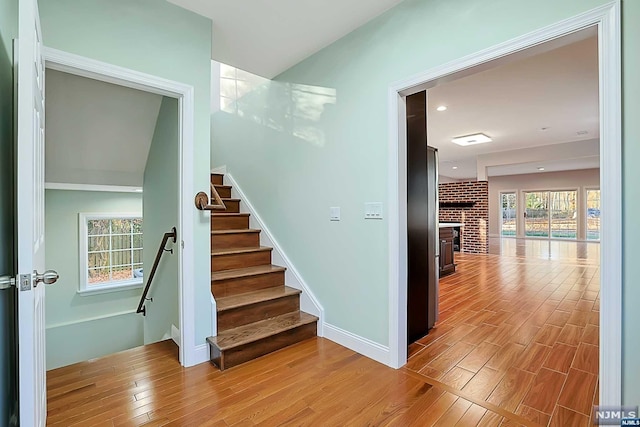 staircase with hardwood / wood-style floors and a brick fireplace