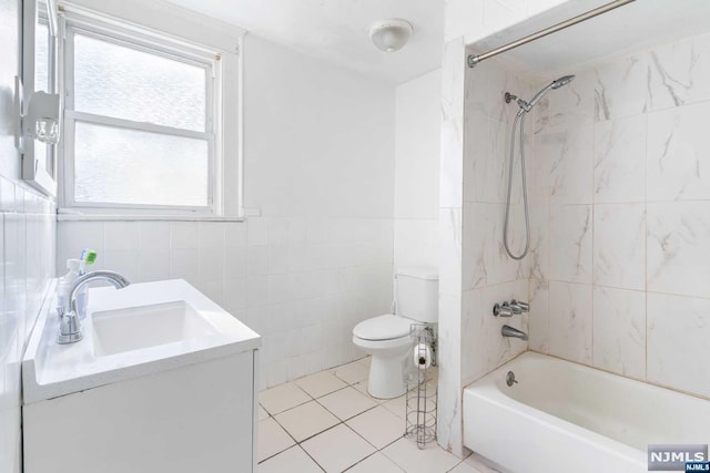 full bathroom with tiled shower / bath combo, tile patterned flooring, toilet, vanity, and tile walls