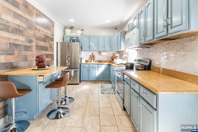 kitchen featuring a breakfast bar, decorative backsplash, stainless steel appliances, and blue cabinetry