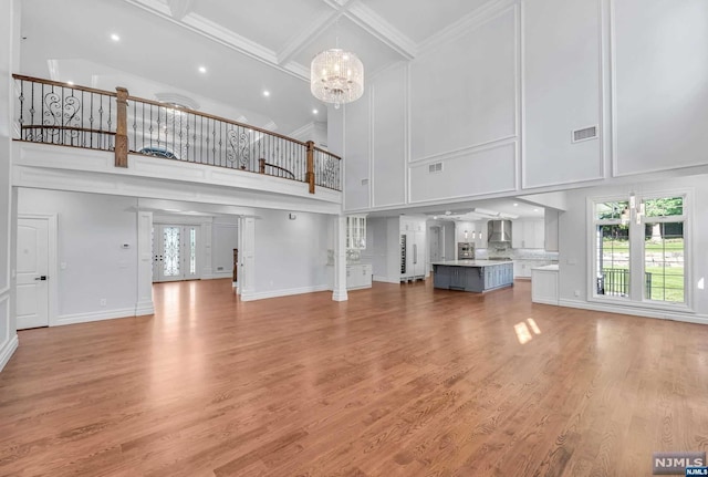 unfurnished living room featuring light wood-type flooring, a towering ceiling, and a chandelier