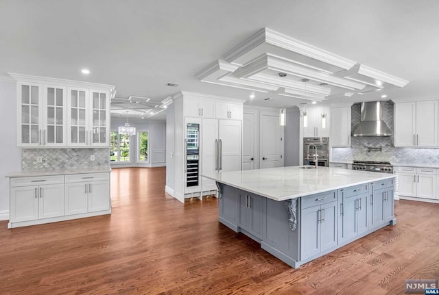 kitchen featuring backsplash, wall chimney range hood, a large island with sink, hardwood / wood-style flooring, and white cabinets