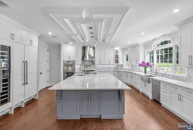 kitchen with a kitchen island with sink, white cabinets, sink, wall chimney exhaust hood, and stainless steel appliances