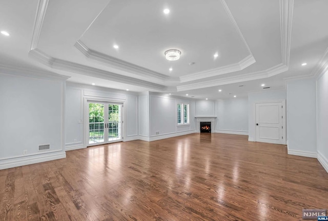 unfurnished living room featuring hardwood / wood-style flooring, a raised ceiling, ornamental molding, and french doors