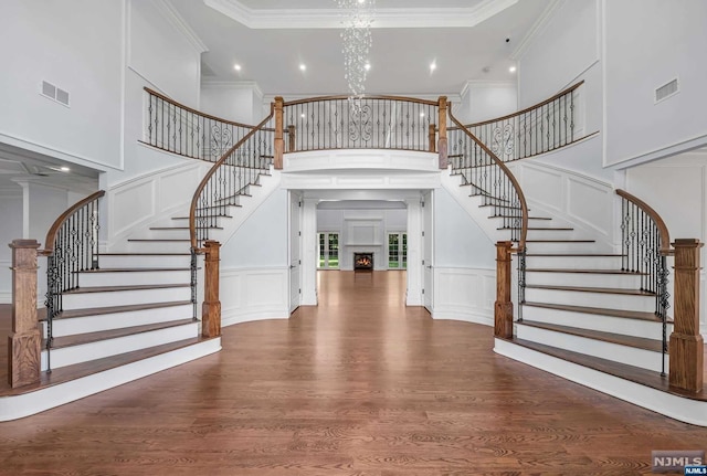 foyer featuring hardwood / wood-style floors, a towering ceiling, a notable chandelier, and ornamental molding