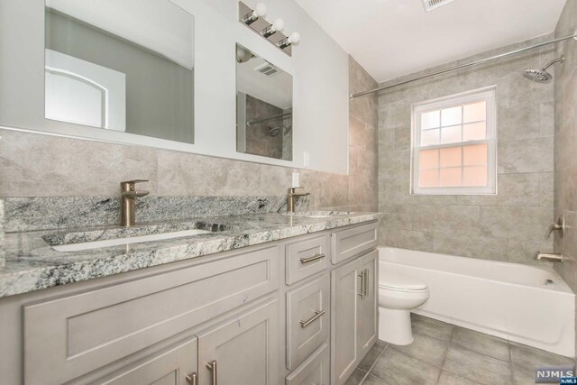 full bathroom featuring tiled shower / bath combo, tile patterned floors, toilet, vanity, and tile walls