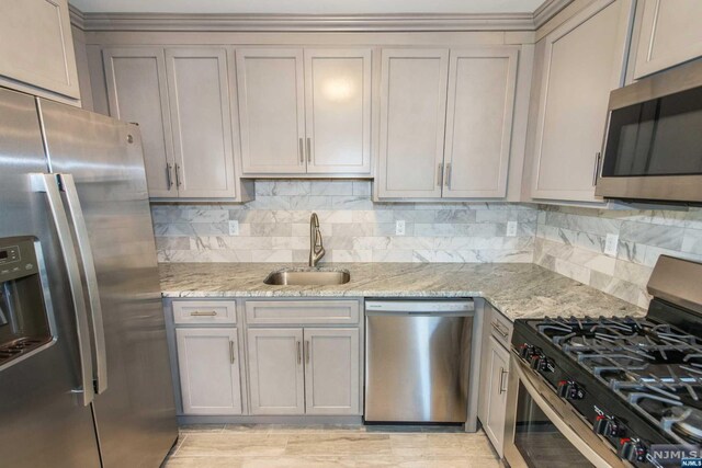 kitchen featuring light stone countertops, appliances with stainless steel finishes, backsplash, and sink