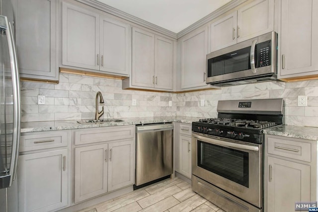 kitchen with appliances with stainless steel finishes, backsplash, light stone counters, sink, and light hardwood / wood-style floors