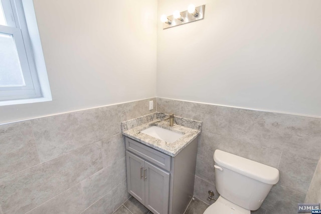 bathroom featuring vanity, toilet, and tile walls