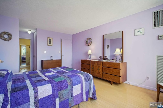 bedroom with ensuite bathroom, a textured ceiling, and light hardwood / wood-style flooring