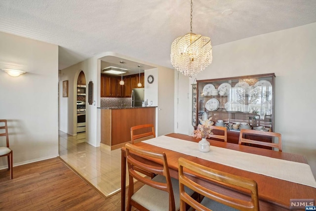 dining area with wood-type flooring, a textured ceiling, and a notable chandelier