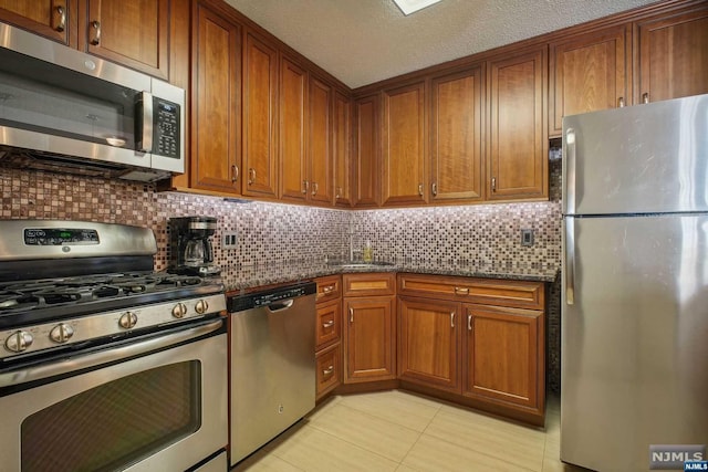 kitchen with dark stone counters, decorative backsplash, a textured ceiling, appliances with stainless steel finishes, and light tile patterned flooring